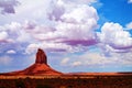 Butte rock formation from ground level with scrub bushes and fluffy clouds in Monument Valley, Arizona