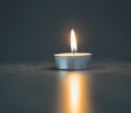 Single tea light candle on the blurred grey background