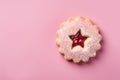 Single traditional Linzer Christmas cookie with shortcrust pastry and jam filling on pink background with copy space