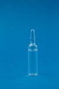 Single transparent glass ampoule with medicine on a blue background