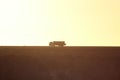 a single truck traveling on a dirt road with sunset in the background