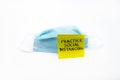 Single use medical face mask with handwritten message on post-it note Practice Social Distancing isolated over white background,