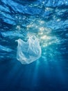 Single-use plastic bag floating underwater illuminated by sunlight rays showcasing ocean pollution and environmental impact of Royalty Free Stock Photo
