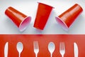 Single use white plastic cutlery and red plastic glass on a red and white background. Concept: Ban single use plastic Royalty Free Stock Photo