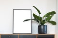 Single vertical black fram with white mockup area next to green potted plant on Scandinavian design sideboard against white wall