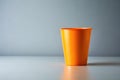 A single vibrant orange plastic cup sits on a smooth, light gray surface against a muted gray background. Generative AI Royalty Free Stock Photo