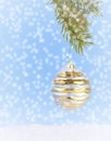 A single, vintage Christmas ornament hanging from a branch of Christmas tree above artificial snow on a blue background.