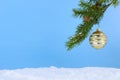 A single, vintage Christmas ornament hanging from a branch of Christmas tree above artificial snow.