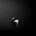 A single water droplet rests on a smooth, dark surface, creating a high-contrast Royalty Free Stock Photo