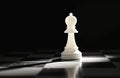 Single white bishop chess piece isolated on dark background, standing on black and white checkered board. Light shines on piece Royalty Free Stock Photo