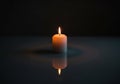A single white candle is lit on a dark surface, casting a warm glow Royalty Free Stock Photo