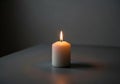 A single white cylindrical candle is lit on a dark grey surface. The flame is small and pointed, Royalty Free Stock Photo