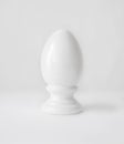 Single white decorative ceramic statuette egg in egg-cup on white table top background. Easter religious Christian symbol. Royalty Free Stock Photo