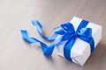 Single white gift box with blue ribbon on wood table close up Royalty Free Stock Photo