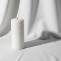 A single white pillar candle stands lit on a white fabric drape Royalty Free Stock Photo