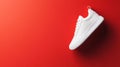 A single white sneaker is positioned against a bright red backdrop, highlighting its clean lines and contemporary design elements Royalty Free Stock Photo