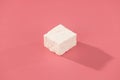 a sugar cube on top of a pink background, with a shadow on the side