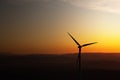 Single wind turbine is silhouetted against an orange sunset sky. Royalty Free Stock Photo