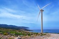 Single windmill turbine on hilltop of seashore in colorful landscape against dynamic blue sky with clouds and winding