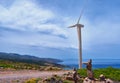 Single windmill turbine, road and balancing stones on hilltop of seashore in colorful landscape at dynamic blue sky on Royalty Free Stock Photo