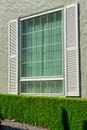 Single window with white shutters and beige stucco exterior walls with front yard shrubs in urban or suburban city Royalty Free Stock Photo