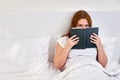 A single woman reads a book lying alone in a double bed. Family relationships in isolation due to coronavirus Royalty Free Stock Photo