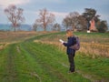 A single woman walker in walking gear on a route through a cut field of crop stubble checks her route with a map.