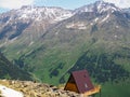 Single wooden house with a red roof on a hill high in the mountains with a beautiful view of the green valley on a Sunny day Royalty Free Stock Photo