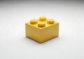 A single yellow Lego brick with four studs sits on a white background {Ai generated Royalty Free Stock Photo