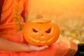 A sinister Halloween pumpkin in the hands of a girl in an orange dress
