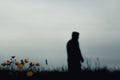 A sinister hooded figure standing in a field, out of focus. With a low camera angle. With Buttercups in the foreground