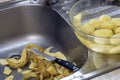 In the sink, next to a bowl of peeled potatoes, is a knife with a potato skin. Selective focus Royalty Free Stock Photo