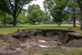 sinkhole forming in the middle of a park, with debris and mud visible