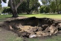 sinkhole forming in the middle of a park, with debris and mud visible