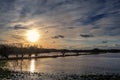 Sinking sun with reflection in the water and a cloudy sky over a dark wetland landscape on a winter evening, Baltic Sea near Royalty Free Stock Photo