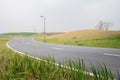 Sinuous asphalted road on grassy acclivity in light winter mist Royalty Free Stock Photo