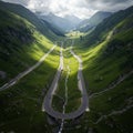 A sinuous mountain road winds through lush green valleys, under a cloudy sky. The Royalty Free Stock Photo