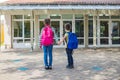 Sister and brother return to school after vacation. Children hold hands in front of school doors. The new school year