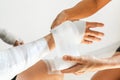 Sister wrapping her brother wrist and arm with bandage around injured hand over white background at home Royalty Free Stock Photo