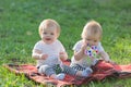 Sisters babies in light clothes sit in the park on the grass without parents