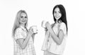Sisters or best friends in pajamas. Morning coffee concept. Blonde and brunette on smiling faces holds mugs with coffee