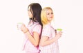 Sisters or best friends in pajamas stand back to back. Blonde and brunette on sleepy faces holds mugs with coffee. Girls