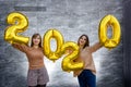 Sisters celebrating new 2020 year. They holding golden air balloons at party celebration Royalty Free Stock Photo