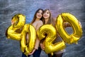 Sisters celebrating new 2020 year. They holding golden air balloons at party celebration Royalty Free Stock Photo