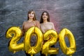 Sisters celebrating new 2020 year. They holding golden air balloons at party celebration Royalty Free Stock Photo