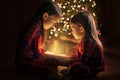 The sisters are holding a box with a magical glow from the inside sitting on the floor by the Christmas tree. Royalty Free Stock Photo