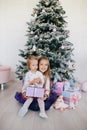 Sisters at home with Christmas tree and presents. Portrait of happy children girls with Christmas gift boxes and decorations.