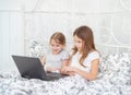 Sisters play on computer online at home bed.