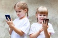 Sisters, young children using modern smartphones, two girls together holding and using their mobile phones, playing around Royalty Free Stock Photo