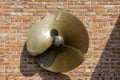 A brass propeller from a launch on a brick wall background.